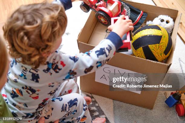 little boy pouring toys into a box for donation - carton box stockfoto's en -beelden