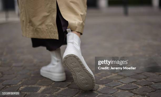 Carmen Kroll wearing brown COS satin slip dress, beige Edited Trenchcoat and white Copenhagen Studios boots on May 11, 2021 in Cologne, Germany.