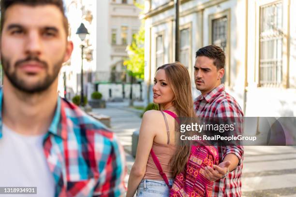 disloyal young  woman looking another man and her angry boyfriend looking at her on the street - cheating boyfriend stock pictures, royalty-free photos & images