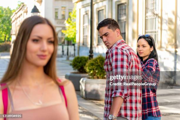 infidelity concept. unfaithful womanizer guy turning around amazed at another woman while walking with his girlfriend on street - meme imagens e fotografias de stock
