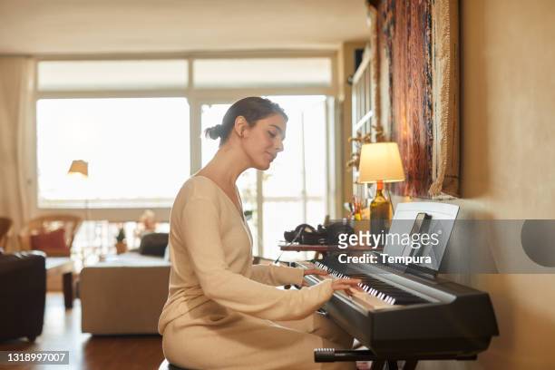 young woman at home playing the piano. - practicing piano stock pictures, royalty-free photos & images