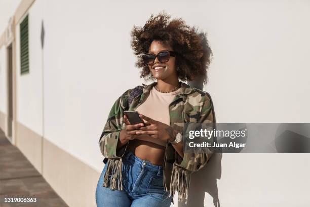 black woman with smartphone resting near wall - stylish woman streets europe cellphone stockfoto's en -beelden