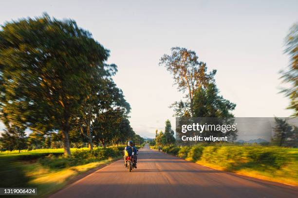 rear view motion image of people on the back of a fast motorcycle transportation in a rural scene malawi - fast motion stock pictures, royalty-free photos & images