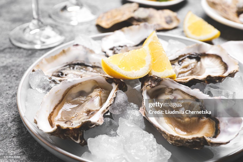 Fresh oysters with lemon and ice on grey table, closeup
