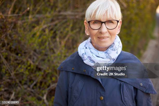 porträtfotos einer 60-jährigen frau mit brille und blonden haaren im freien fotografiert - 63 year old female stock-fotos und bilder