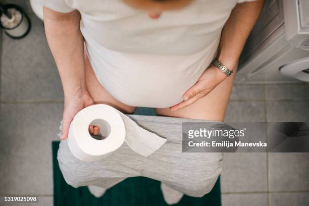 pregnant woman holding toilet paper and using toilet - woman in bathroom stock pictures, royalty-free photos & images