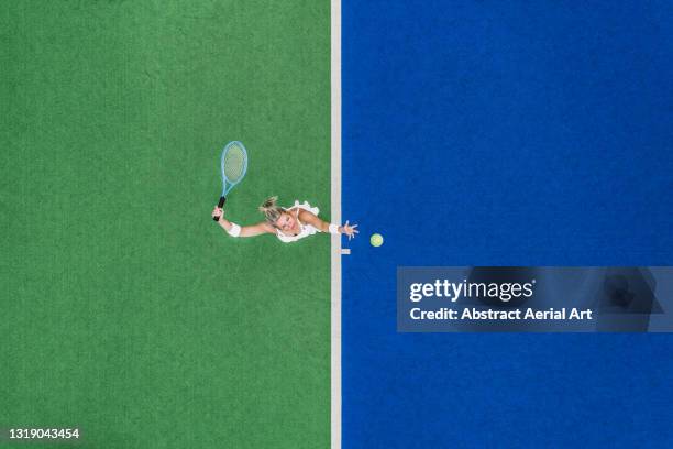 drone shot looking down on a female about to hit a tennis serve on a two-toned, astroturf, tennis court, england, united kingdom - dama game imagens e fotografias de stock