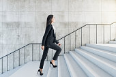 Career success concept with young woman climbs the stairs to the light in abstract building with stylish wall and light stairway.