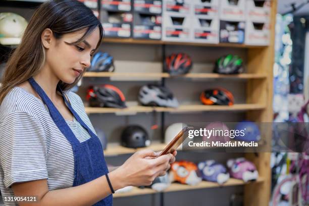 side view of female retail clerk using mobile phone while standing inside bicycle store - sales effort stock pictures, royalty-free photos & images