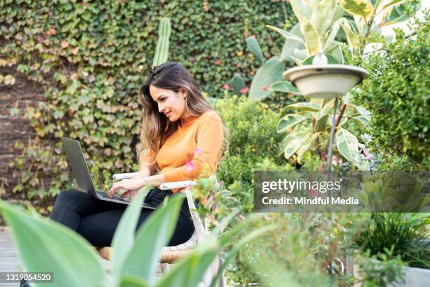 side view of young adult woman sitting on garden using laptop - rooftop deck stock pictures, royalty-free photos & images