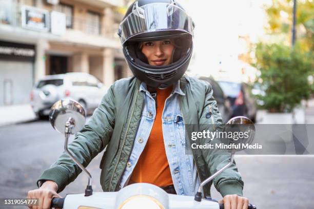 verticale de femme de sourire utilisant le casque de collision tout en s’asseyant sur la moto sur la rue pendant la journée - mobility scooter photos et images de collection