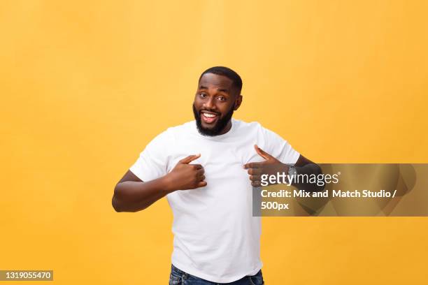 portrait of smiling young man standing against orange background - three quarter length stock pictures, royalty-free photos & images