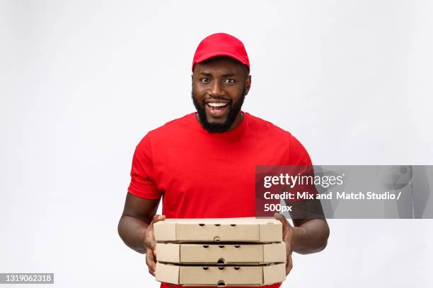 young delivery man holding cardboard box against white background - greasy pizza box stock pictures, royalty-free photos & images