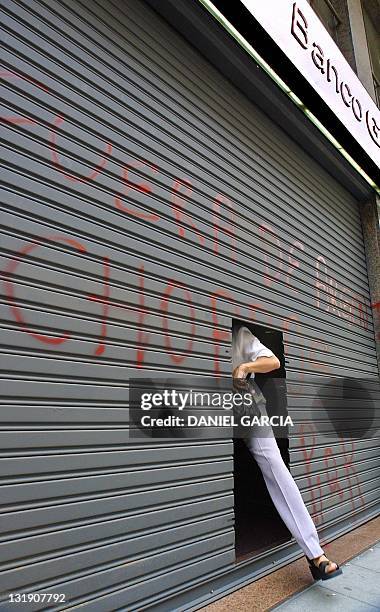 Woman leaves the a bank 21 December 2001 that maintains a closed metal curtain due to the lootings that have plagued the city. At least 26 people...