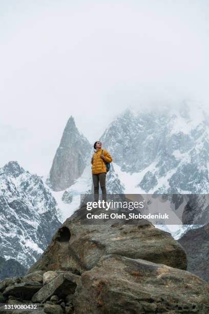 frau steht auf felsen auf dem hintergrund des schneebedeckten bublimotin-gipfels in nordpakistan - hunza valley stock-fotos und bilder