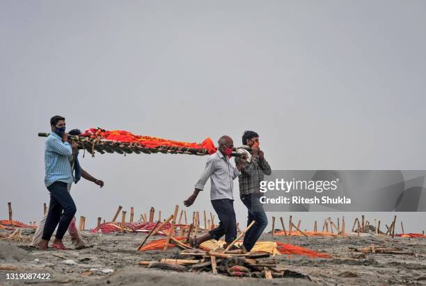 Relatives carry a body for cremation past the graves of people, some of which are believed to be Covid-19 victims, that are partially exposed in...