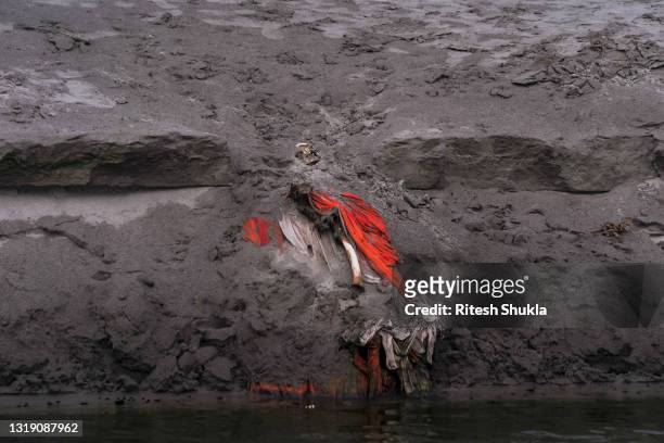 Body lies partially exposed in a shallow sand grave after rains washed away the top layer of sand at a cremation ground on the banks of the Ganges...