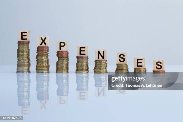 word "expenses" on wooden blocks on top of descending stacks of coins against gray background. - expense stock pictures, royalty-free photos & images