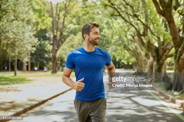 mid adult man is listening to music in park - jogging stock pictures, royalty-free photos & images