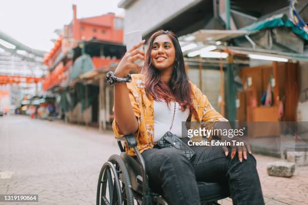 asian indian beautiful woman with disability using wheelchair exploring downtown district in kuala lumpur - indian ethnicity travel stock pictures, royalty-free photos & images