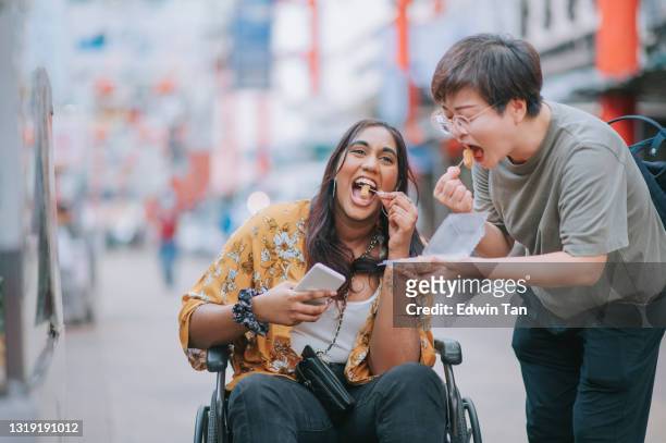 asiatische indische frau mit behinderung sitzen auf rollstuhl genießen mochi lokale street food holding von ihrem chinesischen freund - mochi stock-fotos und bilder