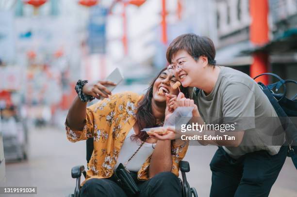 mulher indiana asiática com deficiência sentado em selfie cadeira de rodas desfrutando mochi comida de rua local segurando por seu amigo chinês - visual impairment - fotografias e filmes do acervo