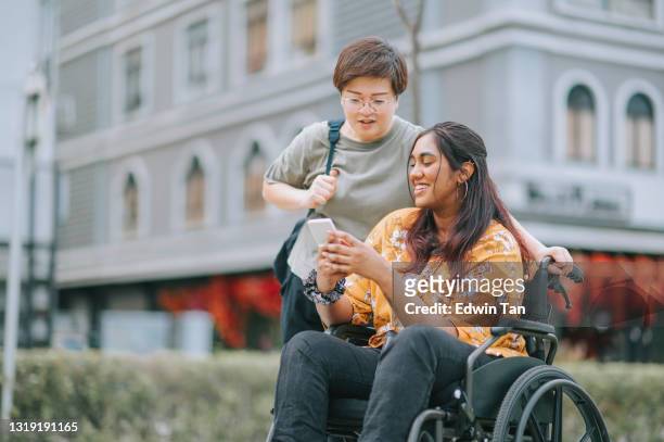 turista asiatica donna indiana con sedia a rotelle che parla con la sua amica cinese sul marciapiede della città - accessibilità foto e immagini stock