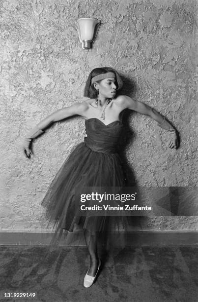 Young person wearing a dress with a tulle skirt and a sweetheart neckline, with a headband and evening gloves, poses with both arms against a...