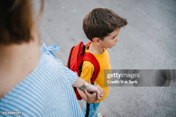 mère tenant la main de son fils le promenant à l’école - enfant cartable photos et images de collection