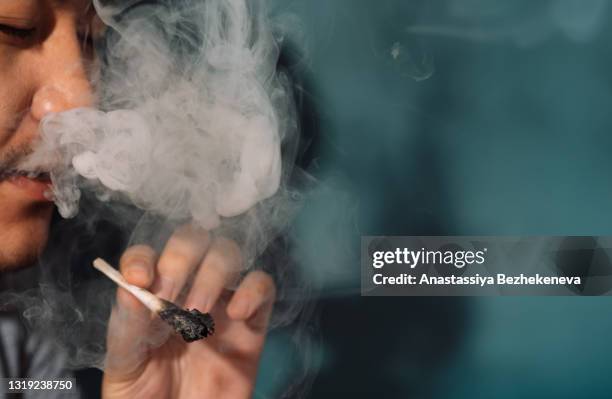 asian smokes cannabis rolls and blows white smoke - smoking weed stock pictures, royalty-free photos & images