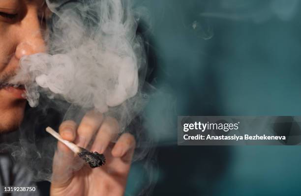 asian smokes cannabis rolls and blows white smoke - cigarette bud stock pictures, royalty-free photos & images