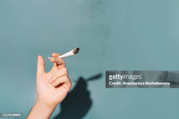 in hand cigarette filled with cannabis against green background - stick stockfoto's en -beelden