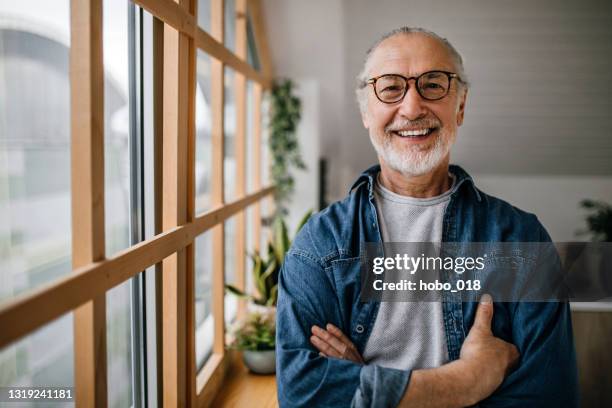 porträt eines hübschen seniors, der neben dem küchenfenster steht - 60 64 jahre stock-fotos und bilder