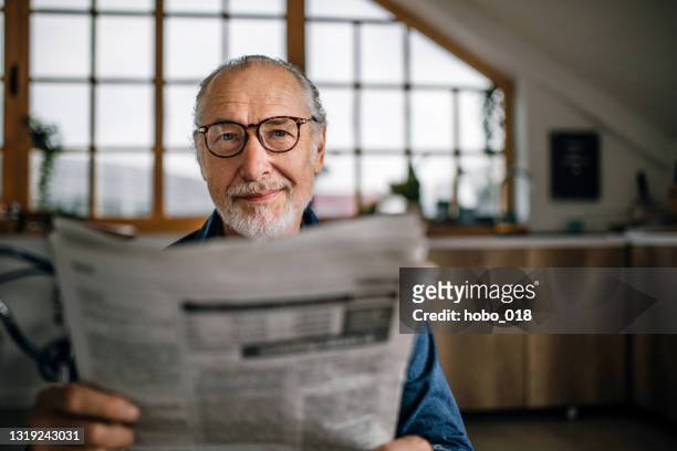homme aîné à la maison affichant des journaux - 60 64 ans photos et images de collection