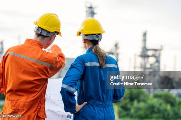 rear view of petrochemical engineers with plan wearing safety coveralls are discussing about production performance of oil and gas. oil and gas industry concepts. - global business continuity stock pictures, royalty-free photos & images