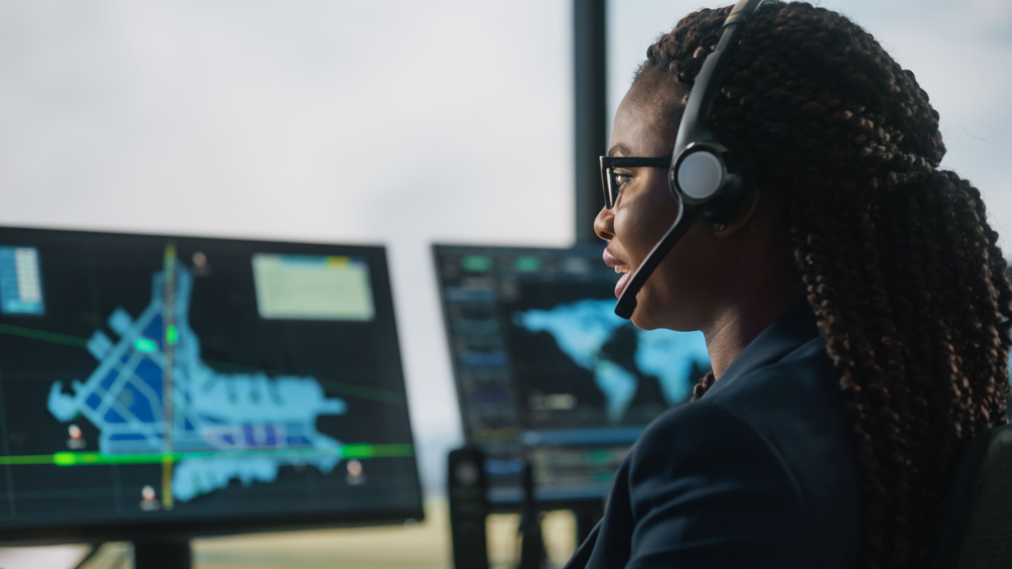 Female Air Traffic Controller with Headset Talk on a Call in Airport Tower. Office Room is Full of Desktop Computer Displays with Navigation Screens, Airplane Departure and Arrival Data for the Team. Female Air Traffic Controller with Headset Talk on a Call in Airport Tower. Office Room is Full of Desktop Computer Displays with Navigation Screens, Airplane Departure and Arrival Data for the Team.
