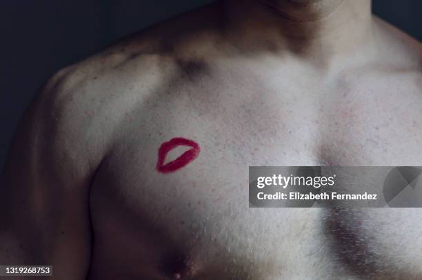 portrait man with lipstick kiss on chest against dark background - verführung stock-fotos und bilder