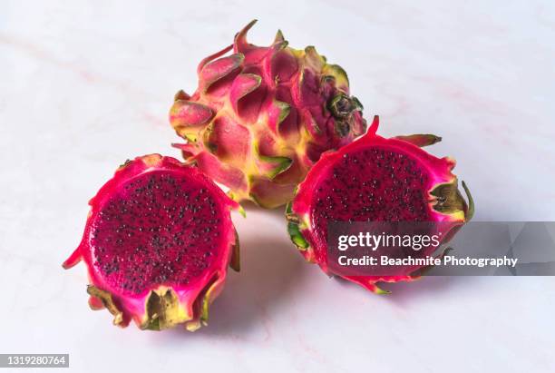 close up of whole and halved dragon fruit or pitahaya/pitaya on pale pink background - röd pitahayafrukt bildbanksfoton och bilder