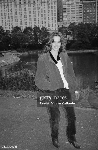 American actress Lea Thompson stands with one hand in the pocket of her blouson-syle jacket, in the background is a lake and the exterior of an...