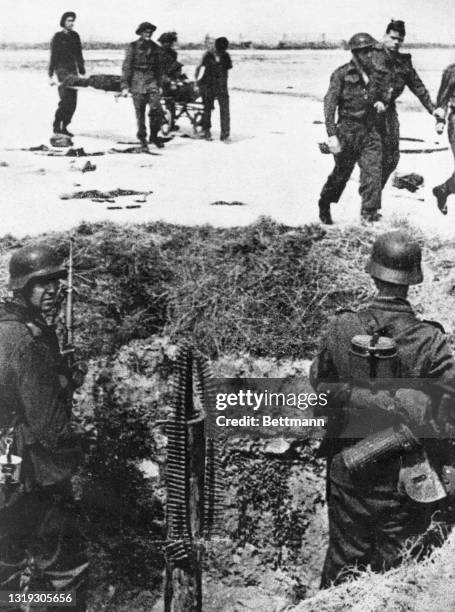 Two German machine gunners watch as Allied soldiers carry off their wounded after the Dieppe raid. The Dieppe Raid took place on August 19, 1942. The...