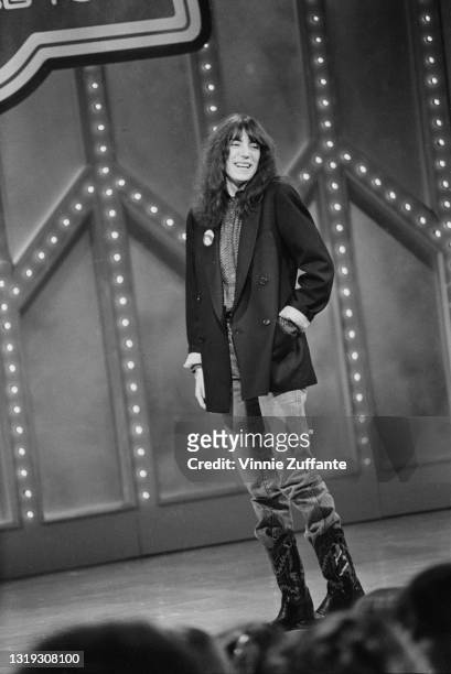 American singer-songwriter, musician and poet Patti Smith, her left hand in the pocket of her black jacket, wearing jeans and cowboy boots, smiling...
