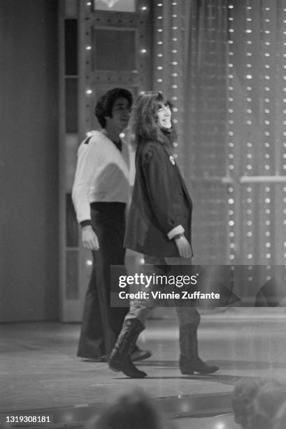 American singer-songwriter, musician and poet Patti Smith, wearing a black jacket, jeans and cowboy boots, smiling alongside an unspecified man on...