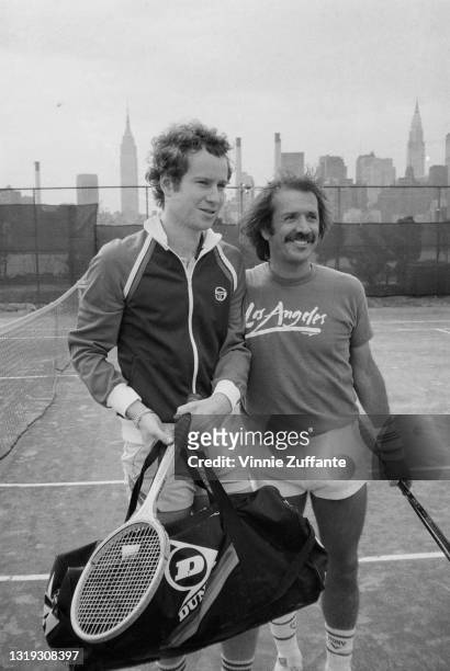 Portrait of American tennis player John McEnroe , in a Sergio Tacchini-branded tracksuit top & white shorts and carrying a Dunlop-branded tennis bag,...