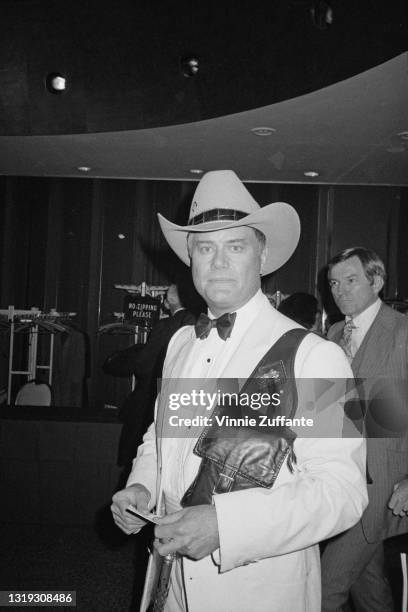 American actor Larry Hagman , wearing a white tuxedo with a black bow tie and a cowboy hat, saddlebags over his shoulder, attends the Night of 100...