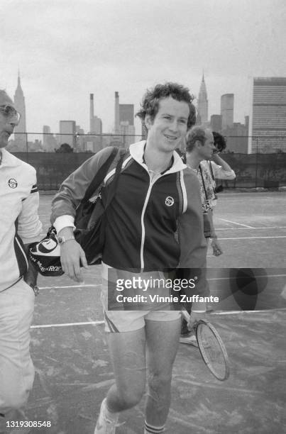 American tennis player John McEnroe, wearing a Sergio Tacchini tracksuit top and white shorts, and carrying a Dunlop tennis bag, at unspecified...