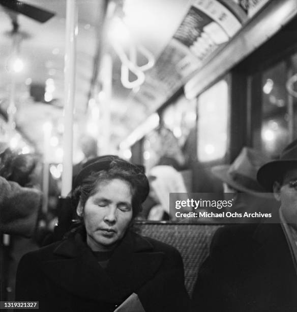 Woman with her eyes closed, possibly sleeping, as commuters and passengers alike travel on the Subway in New York City, New York, December 1948.