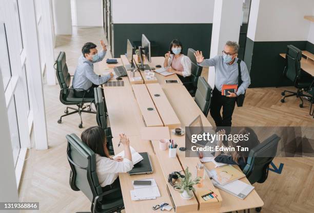 alto ángulo trabajando colega chino senior de nuevo para trabajar con máscara facial saludándose unos a otros en la mañana de la oficina - opening day fotografías e imágenes de stock