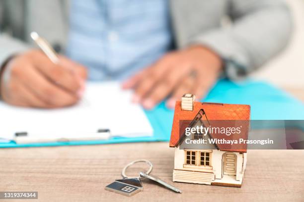 real estate concept - businessman signs contract behind home architectural model - real estate law stock pictures, royalty-free photos & images