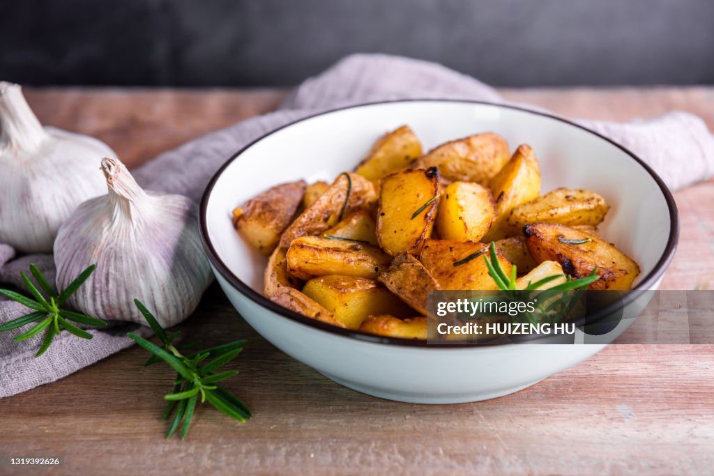 Roasted potatoes with rosemary in a blue bowl on wooden background