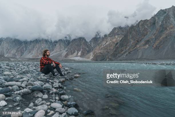 man sitting  on the background of  river and mountains in northern pakistan - beauty in nature stock pictures, royalty-free photos & images